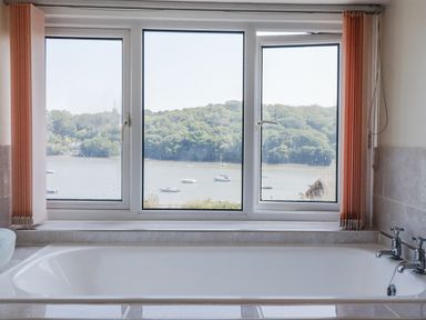 A bathroom with a bathtub and a window overlooking a water view at Kiln Cottage in Golant near Tywardreath