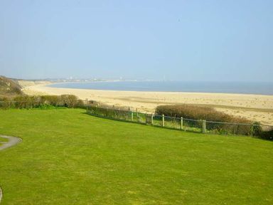 A grassy lawn with bushes and a fence overlooking a sandy beach and the sea at Seascape in Kessingland near Lowestoft