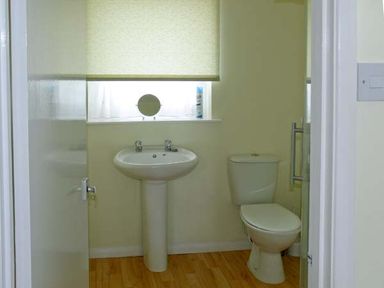 A bathroom with a pedestal sink and a toilet with a window above at Seascape in Kessingland near Lowestoft