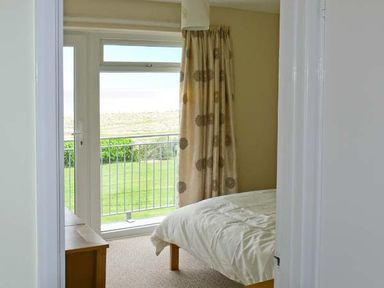 A bedroom with a bed beside a window with curtains overlooking a garden at Seascape in Kessingland near Lowestoft