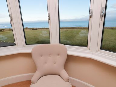 A snug room with a chair and bay windows overlooking the sea at Glen Avon in Seahouses