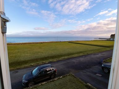 View of the ocean with grass and a car at Glen Avon in Seahouses