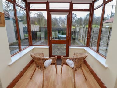 A conservatory with two chairs and a door leading to the garden at Glen Avon in Seahouses