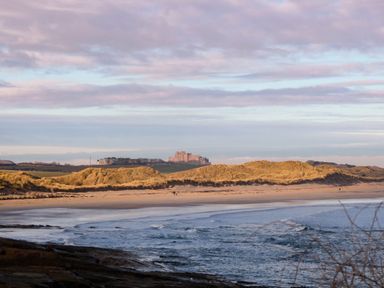 A beach with sand dunes and a castle in the background at Glen Avon, Seahouses