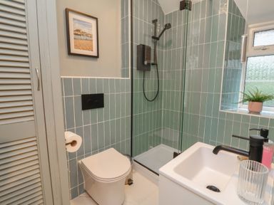 A bathroom with a toilet, shower, sink and a window at Woodedge in Porlock