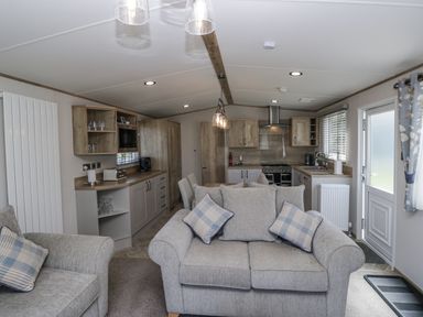 A living room with a sofa and kitchen area at Grasmoor View Lodge