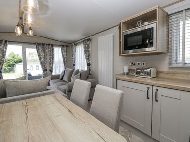 A living room with a dining area and kitchen appliances at Grasmoor View Lodge