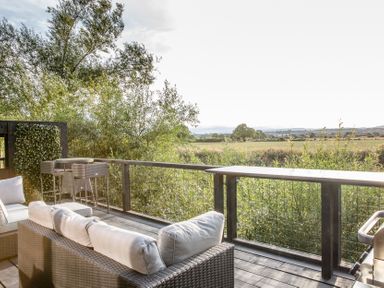 An outdoor patio with a sofa and table overlooking a field at The Larch House in Farndon