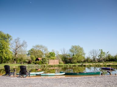An outdoor area with chairs and kayaks by a calm water body at The Larch House in Farndon