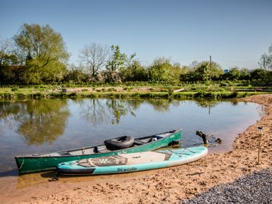 A canoe and a stand-up paddleboard by the water at The Larch House in Farndon