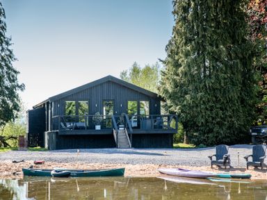 A house with a deck and steps by the water at The Larch House in Farndon