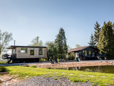 A house with a deck and trees by a lake at The Larch House in Farndon
