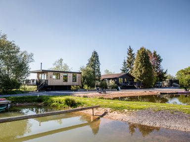 A wooden house with a pond and trees at The Larch House in Farndon