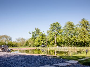 A view of a pond with trees and a boat at The Larch House in Farndon