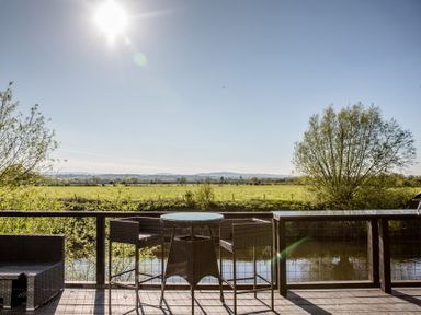 A deck with table and chairs overlooking fields and water at The Larch House in Farndon