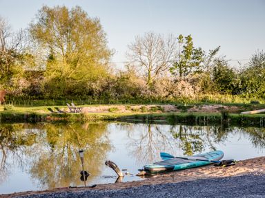 A paddleboard on sandy shore near water with chairs and trees at The Larch House in Farndon