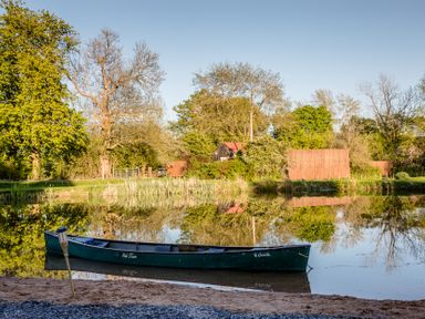 A canoe on water with trees and a building in the background at The Larch House Farndon