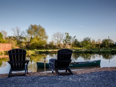 An outdoor seating area by the river with chairs and a canoe at The Larch House in Farndon