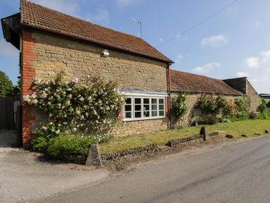 A stone building with flowers and windows at Granary Cottage in Lacock
