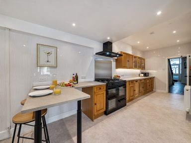 A kitchen with cabinetry, countertop, stove, and bar stools at Clarence House in Llandudno