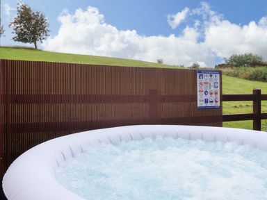 A hot tub with a safety sign and a fence in a grassy area at Badgers Retreat - Two Dales in Richmond