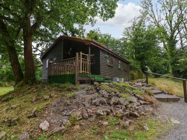 A cabin with a deck surrounded by trees at Oak Lodge near Mynydd Cerrig