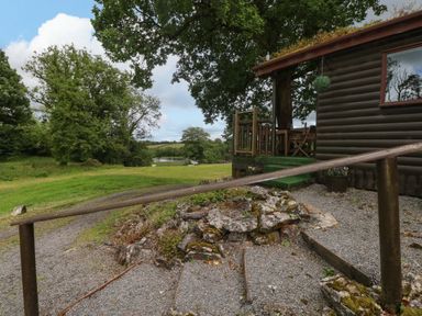 An outdoor view of a cabin with a deck and gravel path at Oak Lodge in Mynydd Cerrig near Porthyrhyd