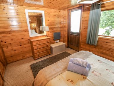 A bedroom with a bed, lamp, and dresser at Oak Lodge near Mynydd Cerrig