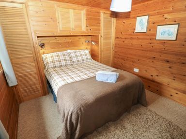 A bedroom with a double bed and wooden walls at Ash Lodge Mynydd Cerrig near Porthyrhyd