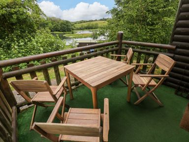 A deck with a table and chairs overlooking water at Ash Lodge in Mynydd Cerrig near Porthyrhyd