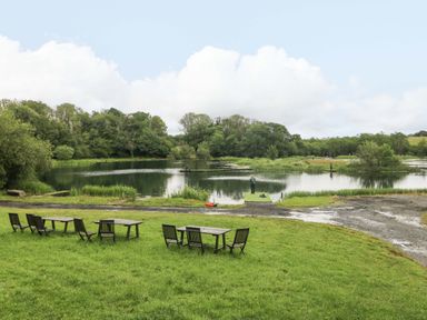 A lake with fishing people and wooden chairs at Ash Lodge near Mynydd Cerrig