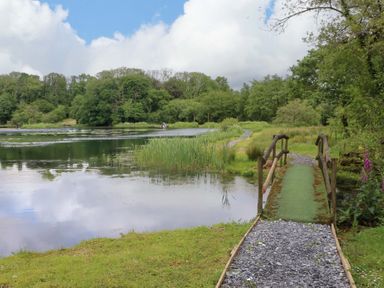 A path and bridge near a lake with trees at Ash Lodge Mynydd Cerrig near Porthyrhyd