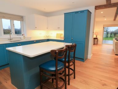 A kitchen with a blue island and bar stools at Peewit Coach House in Moreton-in-Marsh