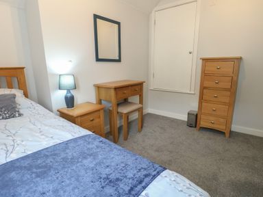 A bedroom with a bed, side table, desk, and dresser at June Cottage in Wool