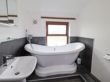 A bathroom featuring a bathtub, sink, and window at Clawddcam in Mathry