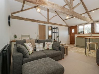 A living room with a sofa and kitchen area at The Old Cart Shed in Gorsley
