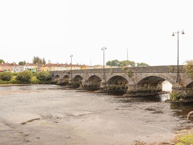A stone bridge over a river with buildings and trees in the background at Shamrock House in Killorglin, County Kerry