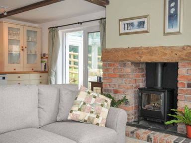 A living room with a sofa facing a fireplace and a glass cabinet at Upper Court Cottage Broad Langdon near Wainhouse Corner