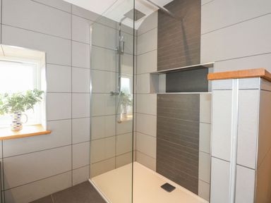 A shower with glass wall and window at Criw in Bryncroes near Sarn Meyllteyrn