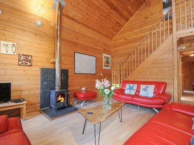 A living room with red sofas, a table, and a stove at Pencarrow in St Breward