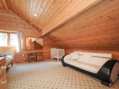 A bedroom with a sofa, crib, mirror, and chest of drawers at Pencarrow in St Breward