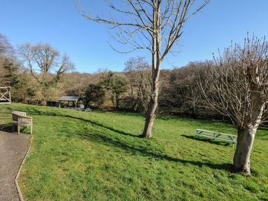 A garden with grass, trees, a bench, and a picnic table at Pencarrow in St Breward