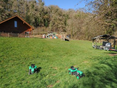 An outdoor area with a house, playground equipment, and ride-on vehicles at Pencarrow, St Breward