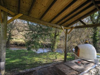 An outdoor cooking area with a shelter and a stream at Trebah in St Breward