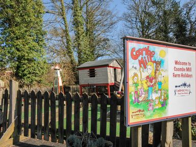 Coombe Mill sign with a playhouse and trees in the background at Coombe Mill in Cornwall