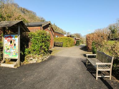 A pathway with a sign and a bench at Coombe Mill in St Breward
