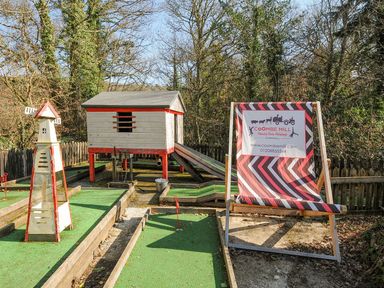 An outdoor play area with a playhouse and windmill at Coombe Mill in Cornwall