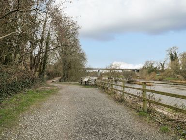 A pathway along a river with a bridge in the background at Cariad Cottage Hereford