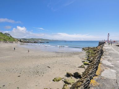 A beach with people swimming and a pier at Mayhurst in Looe