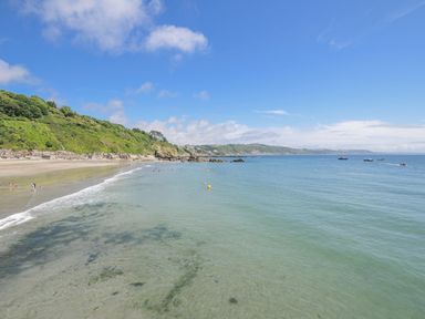 A beach with people in the water and boats near rocks at Mayhurst in Looe
